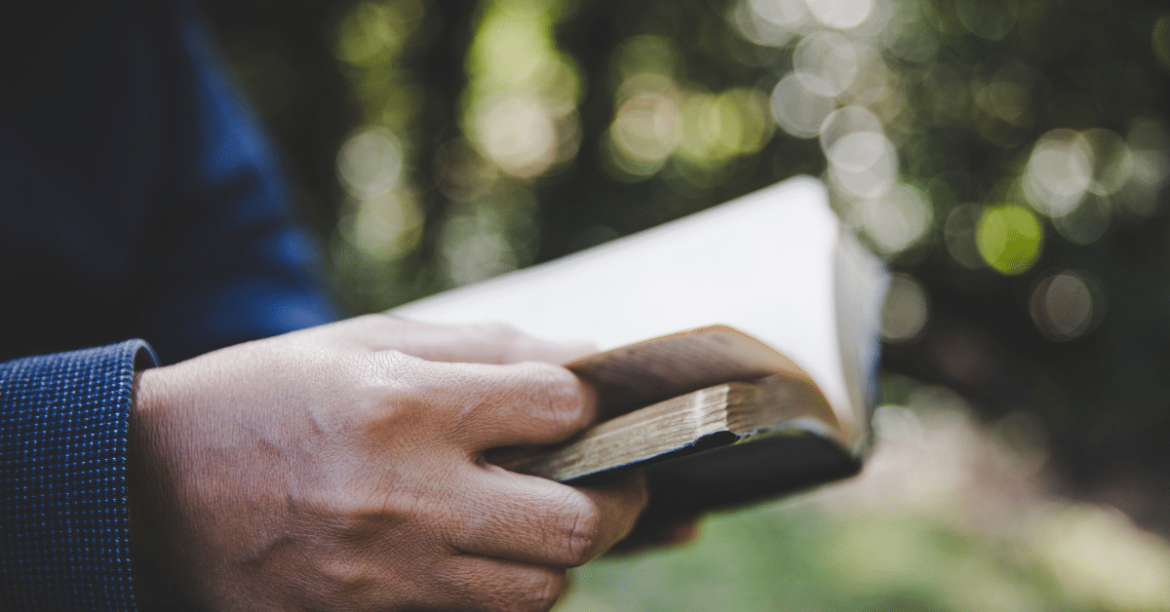 Man-holding-and-reading-Bible-outdoors.png